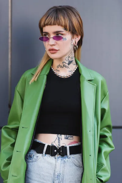 Tattooed woman with piercing looking away near grey wall outdoors — Stock Photo