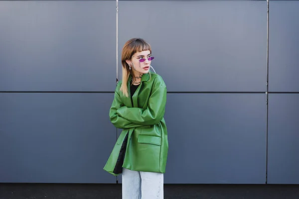Femme tatouée en cuir vert veste debout avec les bras croisés et regardant loin à l'extérieur — Photo de stock