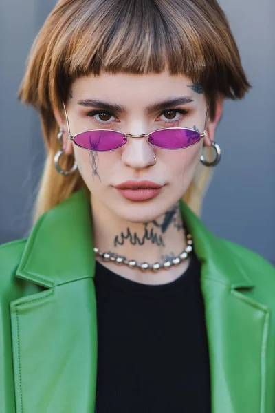 Стильная татуированная женщина в очках смотрит в камеру на улице — стоковое фото