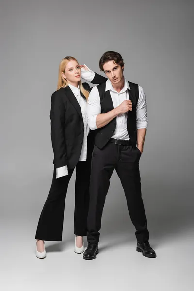 Full length view of stylish couple in elegant clothes looking at camera on grey — Stock Photo