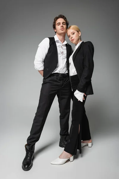 Full length view of elegant couple in black and white clothes posing on grey — Stock Photo