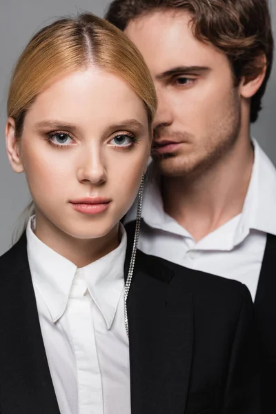 Elegant blonde woman looking at camera near blurred young man isolated on grey — Stock Photo