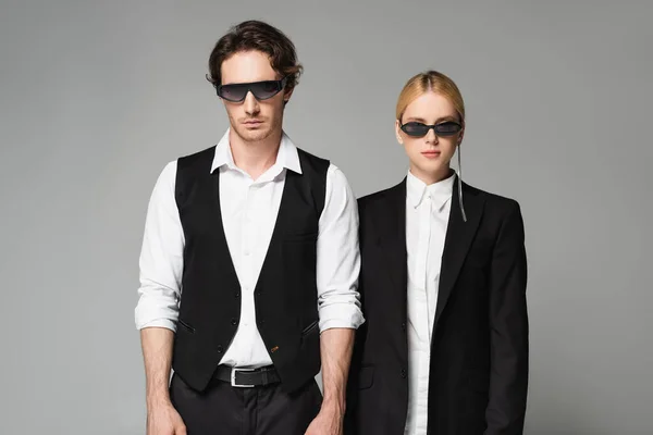Vue de face du jeune couple en lunettes de soleil sombres et vêtements noirs et blancs isolés sur gris — Photo de stock