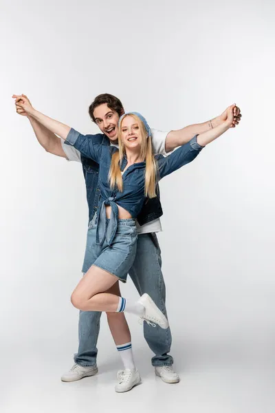 Aufgeregtes Paar in stylischer Jeanskleidung hält Händchen, während es auf Weiß posiert — Stockfoto