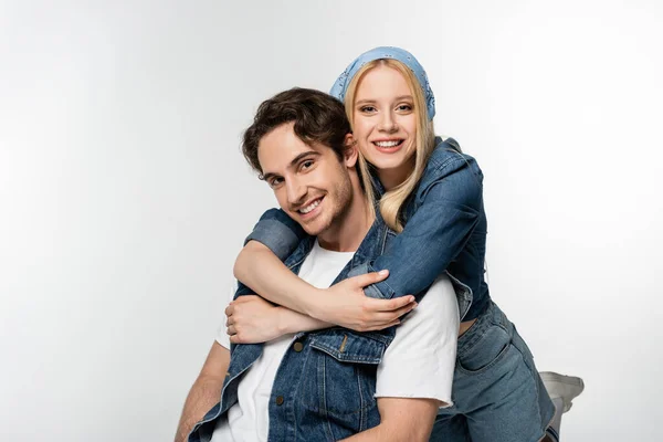 Alegre pareja en denim ropa abrazando mientras sonríe a la cámara aislado en blanco - foto de stock