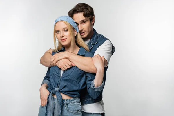 Brunette man embracing trendy woman standing with hand in pocket isolated on white — Stock Photo