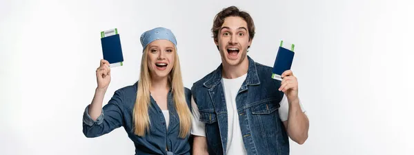 Stylish and amazed couple with travel documents looking at camera isolated on white, banner — Stock Photo