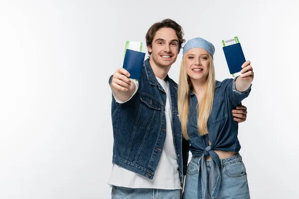 Happy young couple in denim clothes showing passports with air tickets isolated on white — Stock Photo