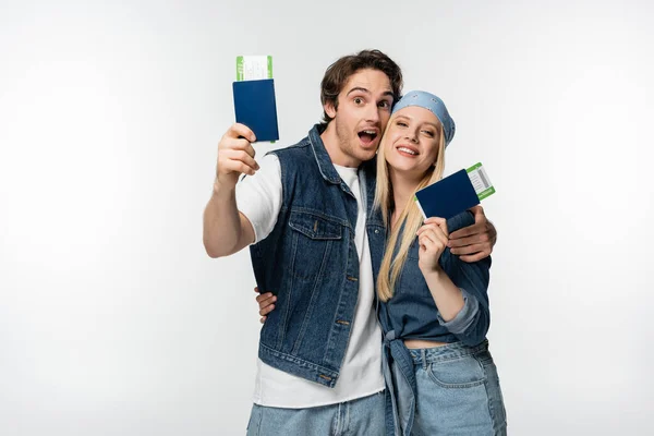 Веселая молодая пара в джинсовой одежде обнимается при предъявлении проездных документов, изолированных на белом — стоковое фото