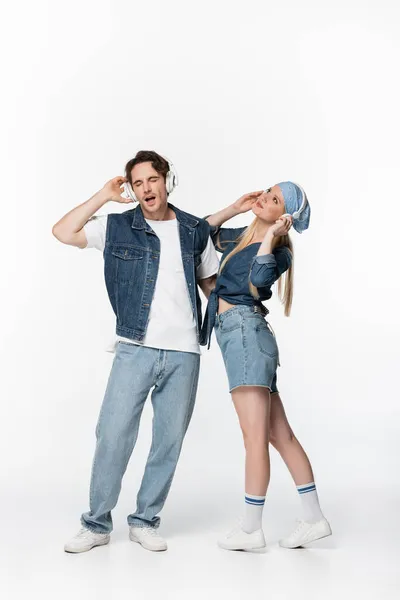 Couple joyeux en denim vêtements écouter de la musique dans les écouteurs sans fil sur blanc — Photo de stock