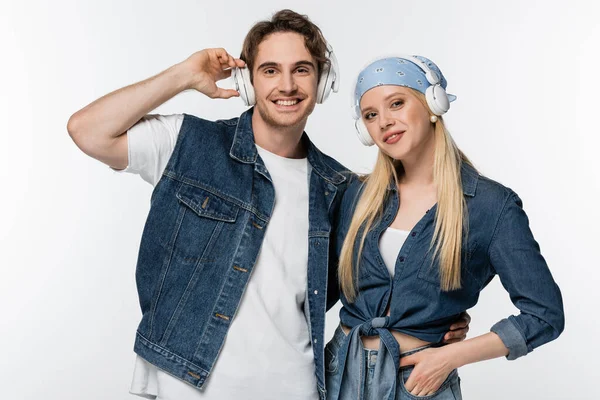 Alegre pareja en ropa de mezclilla escuchando música en auriculares inalámbricos aislados en blanco - foto de stock