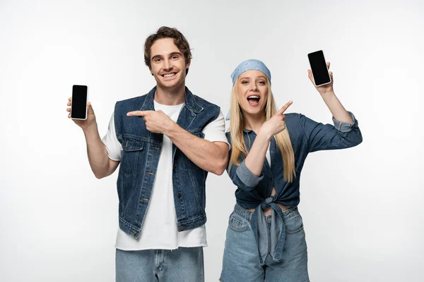 Glückliches stilvolles Paar zeigt auf Mobiltelefone mit leerem Bildschirm isoliert auf weiß — Stockfoto