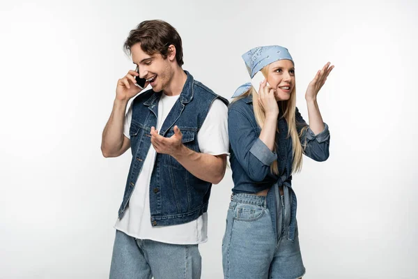 Freudiges Paar in trendiger Jeanskleidung, das auf Mobiltelefonen vereinzelt auf weißem Grund spricht — Stockfoto