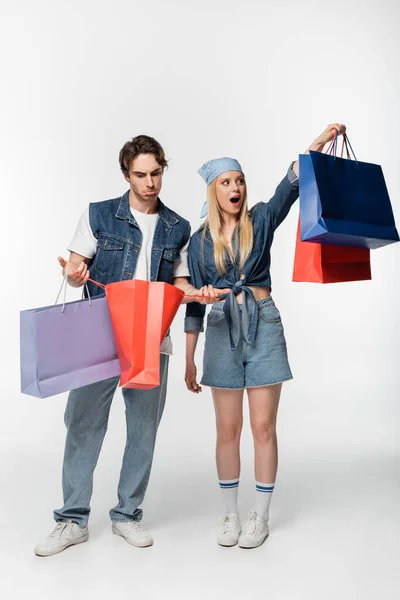 Femme étonnée tenant achats près petit ami surpris regardant dans le sac à provisions sur blanc — Photo de stock