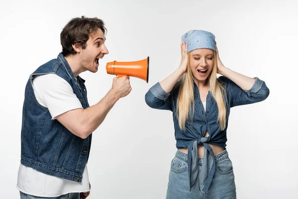 Femme dans bandeau couvrant les oreilles avec les mains près de l'homme criant en mégaphone isolé sur blanc — Photo de stock