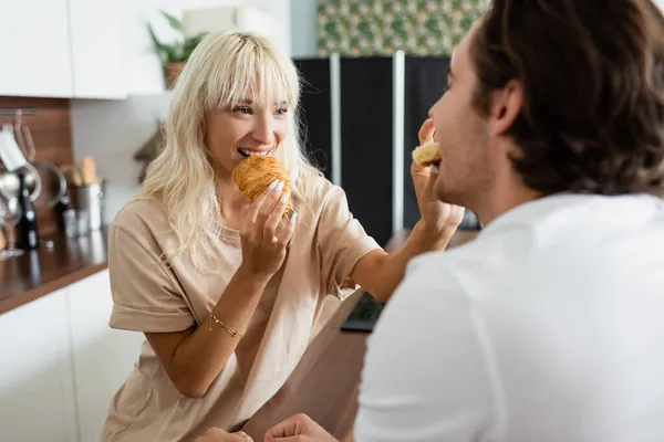 Happy woman feeding blurred boyfriend with tasty croissant — Stock Photo