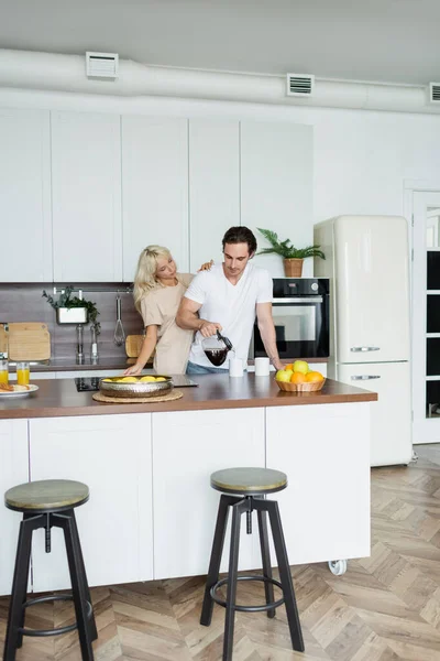 Man pouring coffee into cup near girlfriend in kitchen — Stock Photo