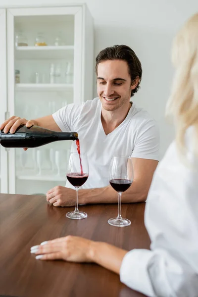 Alegre hombre verter vino tinto en vaso cerca borrosa novia - foto de stock