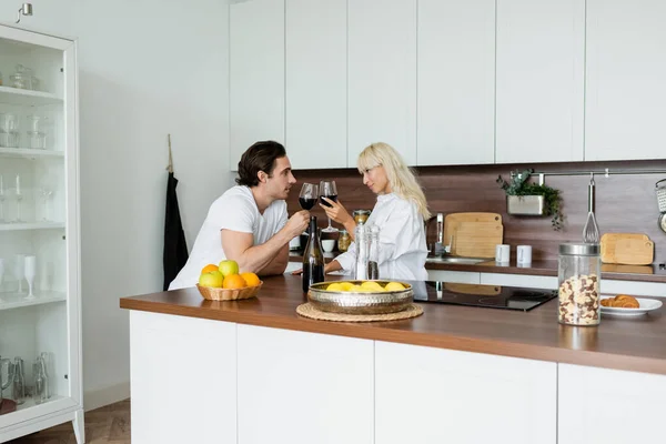Young couple clinking glasses of red wine in kitchen — Stock Photo