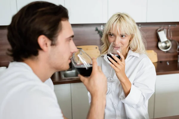 Donna bionda che beve vino rosso e guarda il fidanzato offuscato — Foto stock