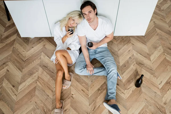 Top view of young man and woman holding glasses of red wine while sitting on kitchen floor — Stock Photo