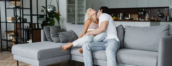 Hombre joven besando cuello de novia rubia con los ojos cerrados en la sala de estar, pancarta - foto de stock