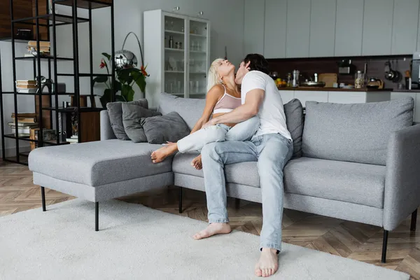 Man kissing neck of blonde girlfriend with closed eyes in living room — Stock Photo
