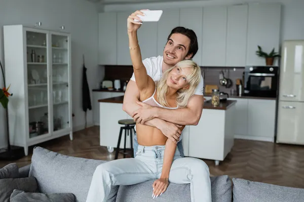 Femme heureuse prenant selfie avec petit ami gai dans le salon — Photo de stock