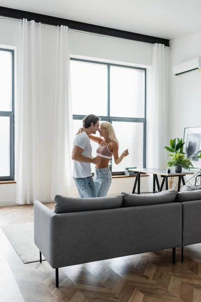 Feliz pareja bailando cerca de sofá gris en la sala de estar - foto de stock