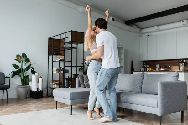 Mujer levantando las manos mientras baila con novio en la sala de estar - foto de stock