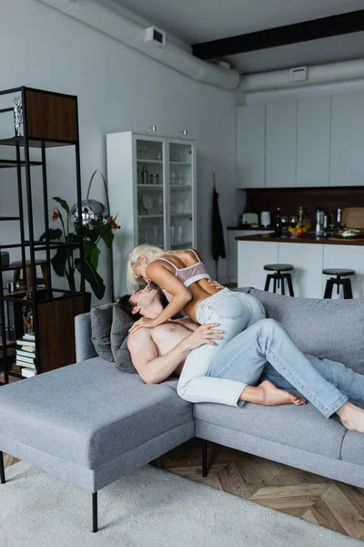 Sexy young woman seducing shirtless man in couch — Stock Photo