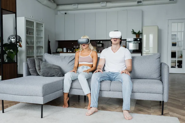 Shocked couple in vr headsets sitting on grey couch — Stock Photo