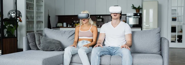 Casal chocado em fones de ouvido vr sentado no sofá cinza, banner — Fotografia de Stock