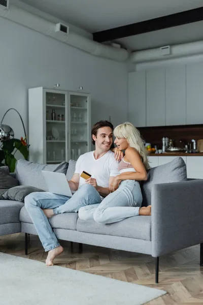 Hombre alegre celebración de la tarjeta de crédito cerca de novia sorprendida mientras que hace compras en línea - foto de stock