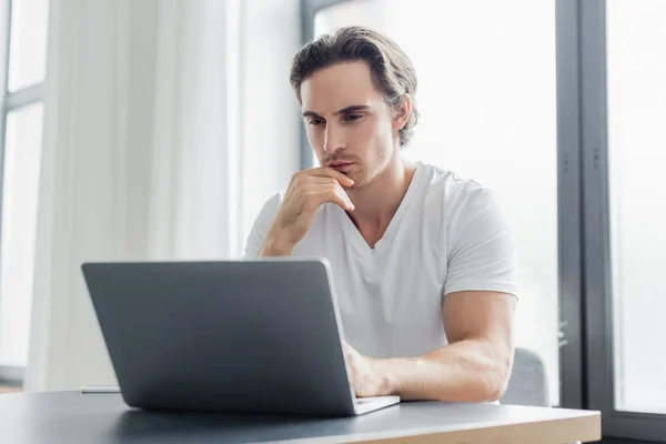 Freelancer enfocado mirando el portátil mientras trabaja desde casa - foto de stock