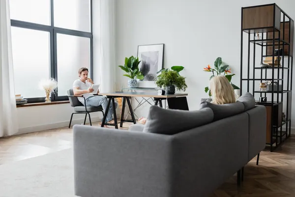 Blonde woman using laptop with blank screen near boyfriend with digital tablet in living room — Stock Photo