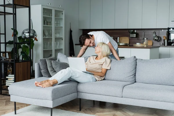 Glücklicher Mann schaut blonde Freundin an, die von zu Hause aus mit Laptop arbeitet — Stockfoto