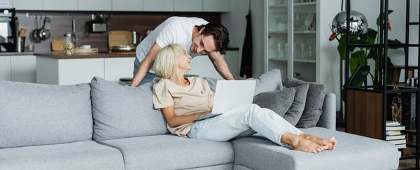 Glücklicher Mann schaut blonde Freundin an, die von zu Hause aus mit Laptop, Banner arbeitet — Stockfoto