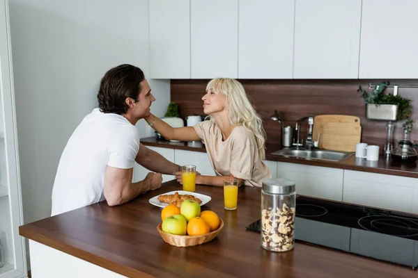 Mujer feliz tocando la cara de novio sonriente en la cocina - foto de stock