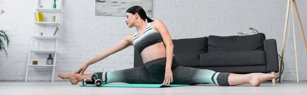 Mujer embarazada en ropa deportiva estiramiento en splits pose en estera de yoga, bandera - foto de stock