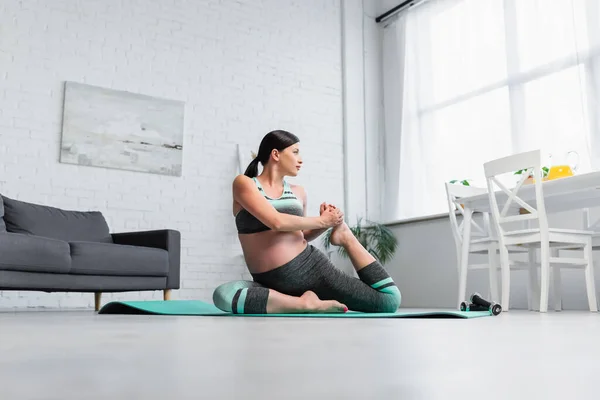 Vista a nivel de superficie de la joven embarazada estirándose en postura de yoga en casa - foto de stock