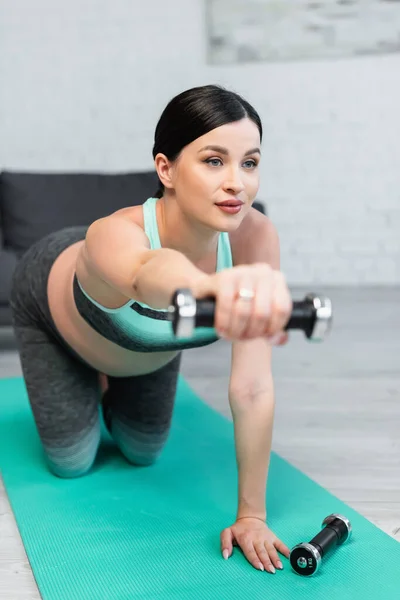 Blurred pregnant woman training with dumbbell while standing on knees on fitness mat — Stock Photo