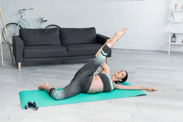 Mujer embarazada estirándose en pose de yoga acostado con la pierna levantada en casa - foto de stock