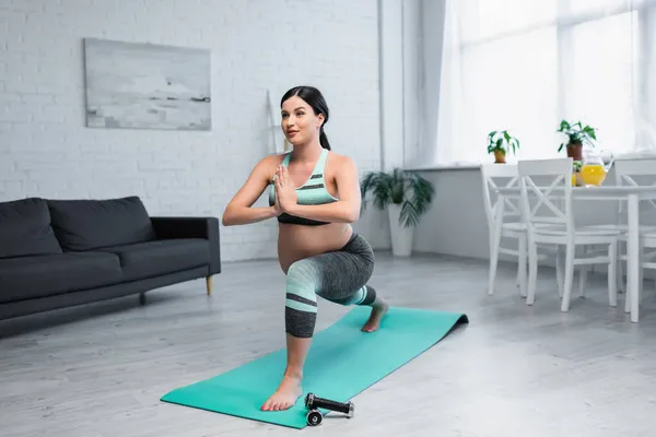 Femme enceinte pratiquant croissant lunge pose avec les mains priantes dans le salon — Photo de stock