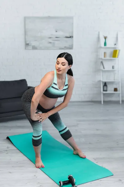 Young pregnant woman warming up on fitness mat at home — Stock Photo