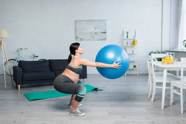 Vue latérale de la femme enceinte faisant des redressements assis avec balle de fitness près de la table avec du jus d'orange frais — Photo de stock