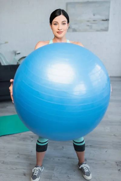 Junge Frau mit Fitnessball blickt beim Training zu Hause in die Kamera — Stockfoto