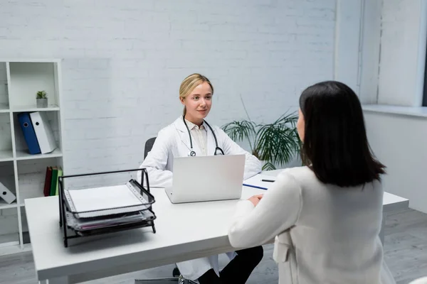 Young doctor listening to brunette woman during appointment in consulting room — Stock Photo