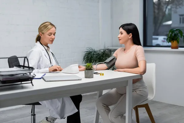 Young doctor measuring blood pressure of pregnant woman in consulting room — Stock Photo