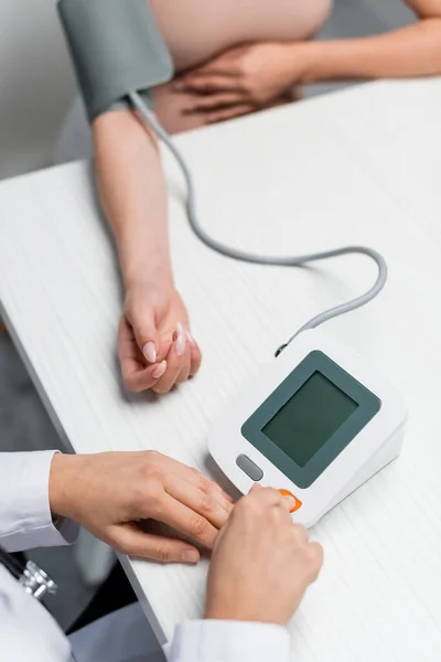 Partial view of doctor measuring blood pressure of pregnant woman on blurred background — Stock Photo